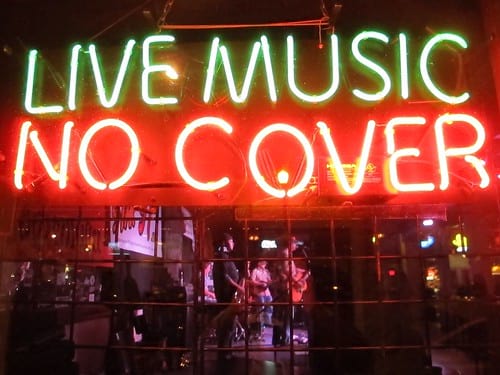 Neon sign that reads Live Music in green and No Cover in red with live band visible through window