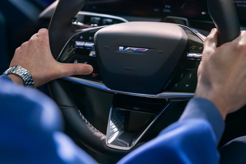 Close-up of a Man About to Press the V-Button on the 2026 OPTIQ-V Steering Wheel | Rydell Cadillac in Grand Forks ND